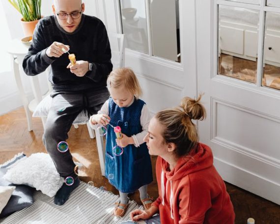 A family bonding while blowing bubbles together indoors, capturing a joyful moment.